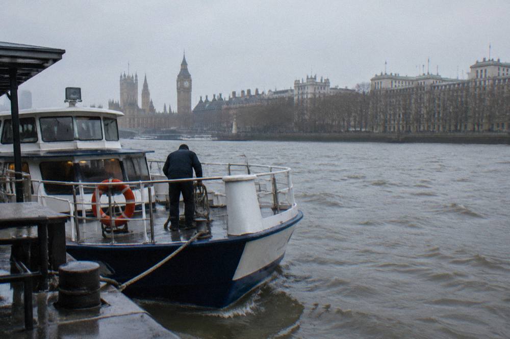 A cruise boat moored at a Thames pier with the London skyline behind it in winter light