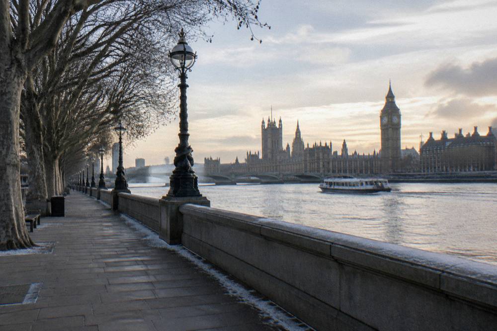 An empty riverside path beside the Thames with a boat passing in the distance on a still winter day