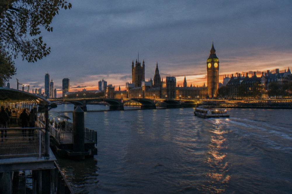A wide view of the Thames at dusk with a lit bridge and the city skyline in the background