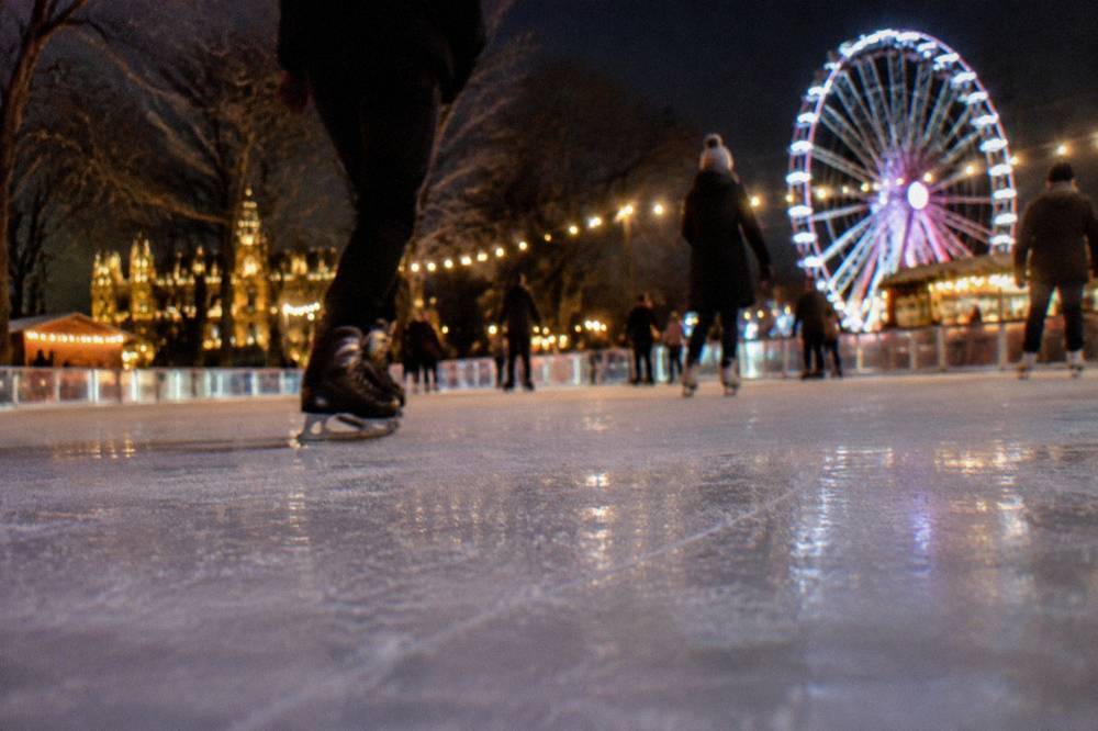 Illuminated ice rink with skaters moving under a canopy of lights beside a fairground wheel