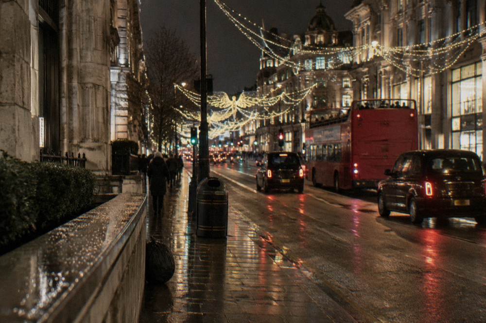 Open-top bus passing under glowing Christmas lights on a London street at night