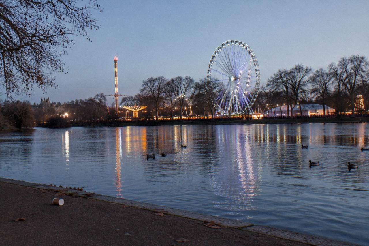 Festively lit fairground rides and a giant wheel glowing above Hyde Park at dusk