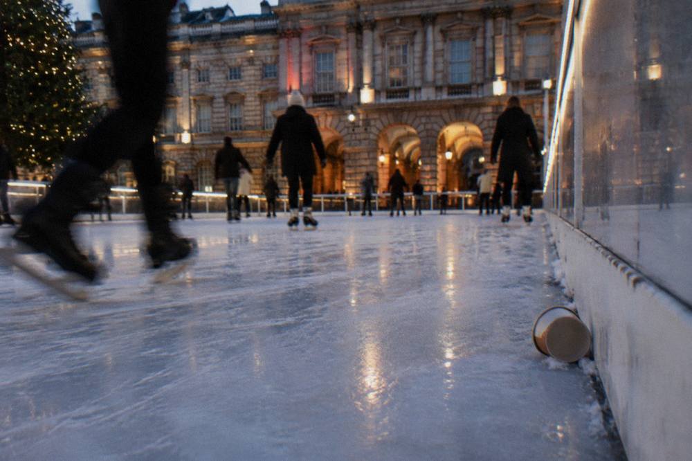 Skaters on an outdoor rink surrounded by stone arches lit for evening