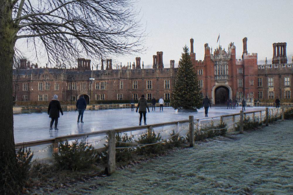 An ice rink in front of a lit historic palace facade with a Christmas tree on the ice