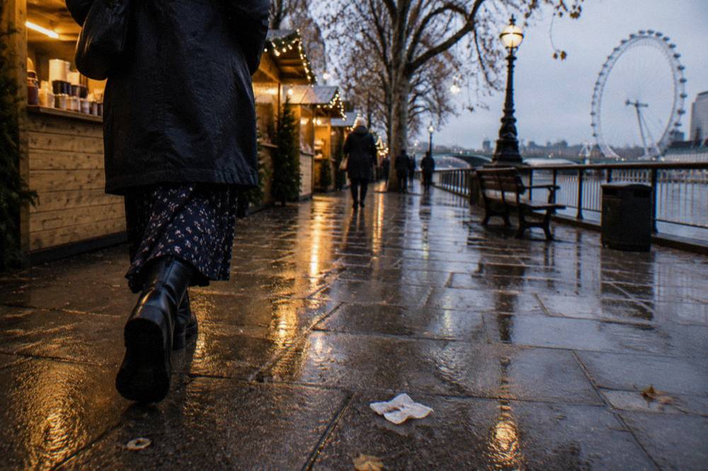 Boots and a rain jacket on a visitor walking past lit Christmas market stalls on wet pavement