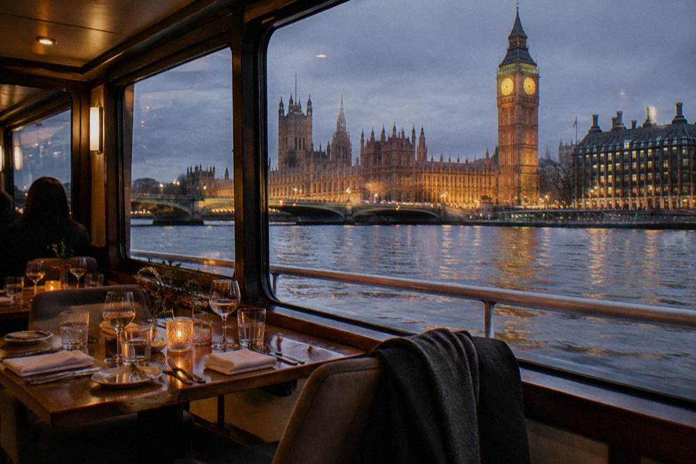Warm interior of a river cruise with set tables and city lights visible through the windows