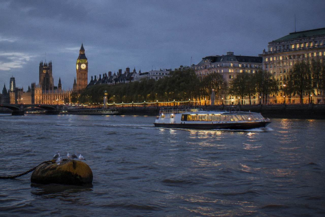 A passenger boat on the River Thames passing illuminated riverside buildings at dusk