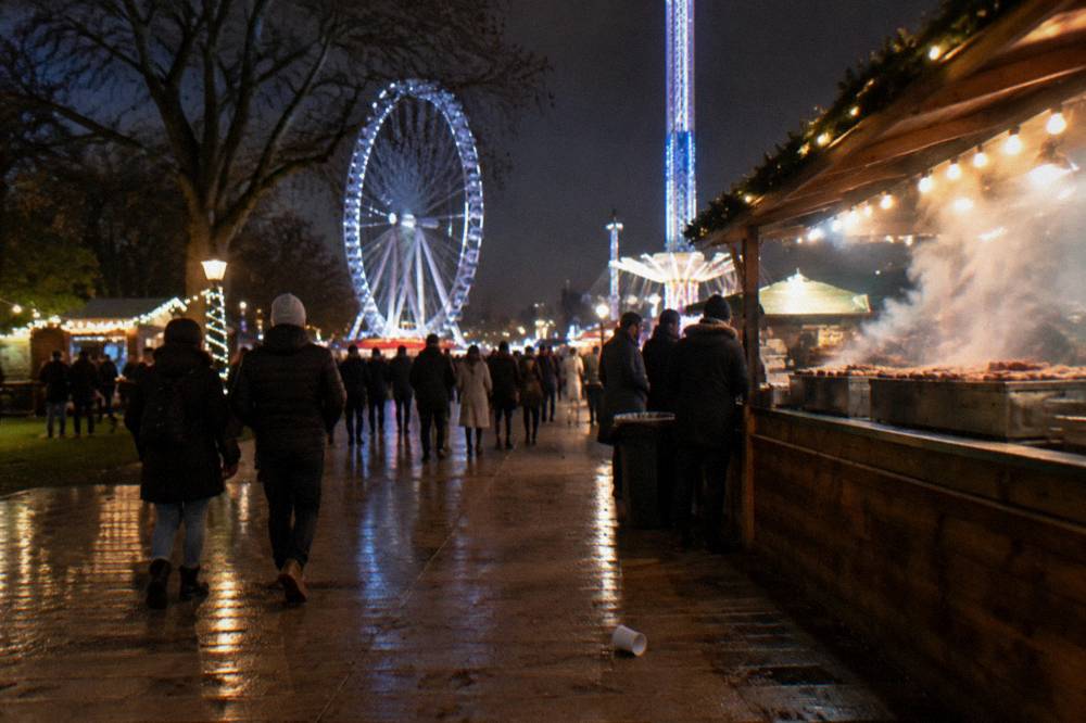 Crowded walkway between food stalls and illuminated ride structures at a winter fair