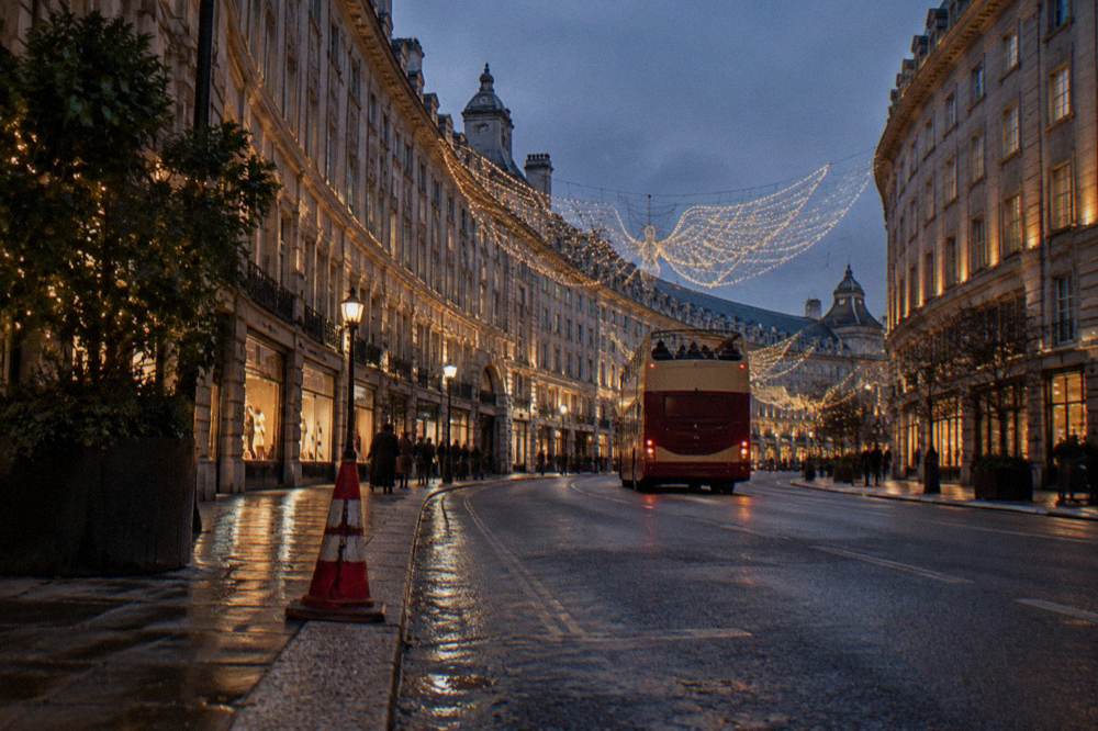 Open-top bus passing illuminated shop fronts on a decorated London street at night