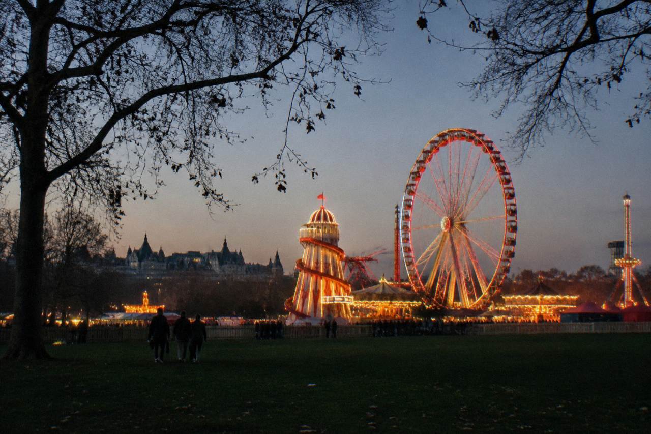 Ferris wheel and fairground rides lit up against an evening sky in a London park