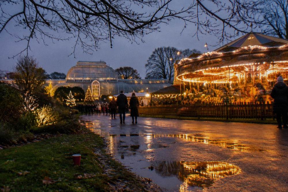 Festive fairground ride glowing beside a lit path at a night garden trail