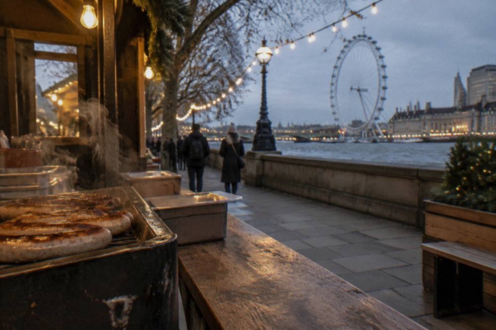 Christmas market stalls with warm lights beside the Thames at dusk