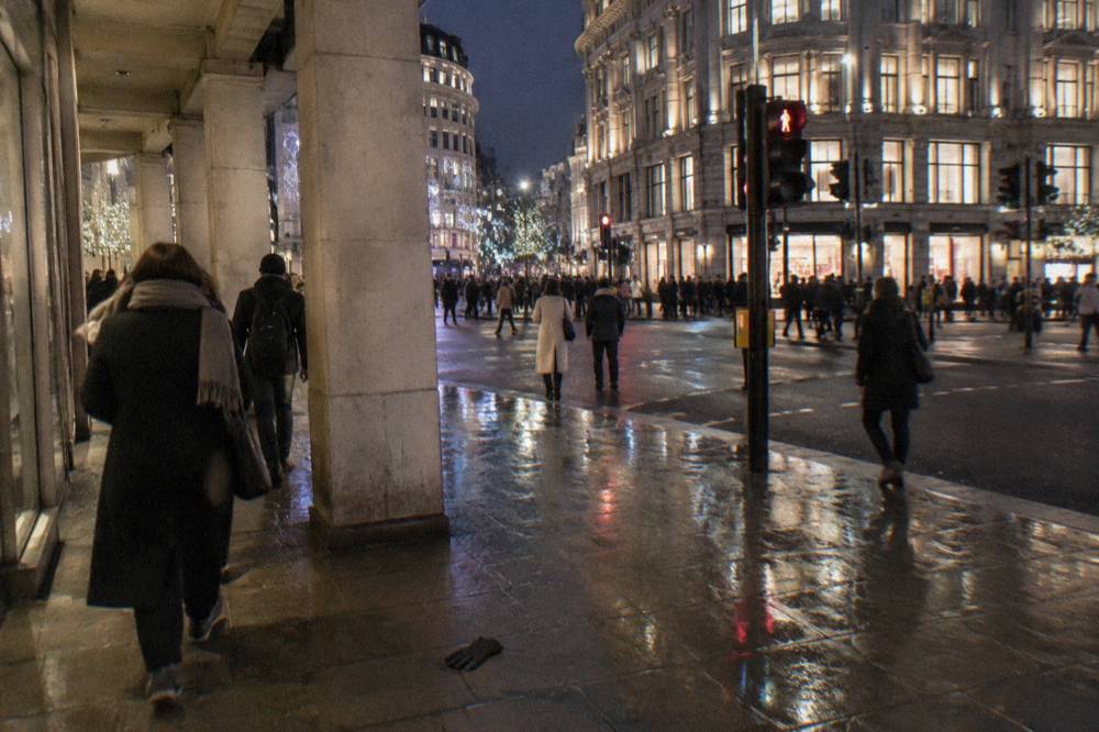 Shoppers in coats and scarves on a decorated London street after dark
