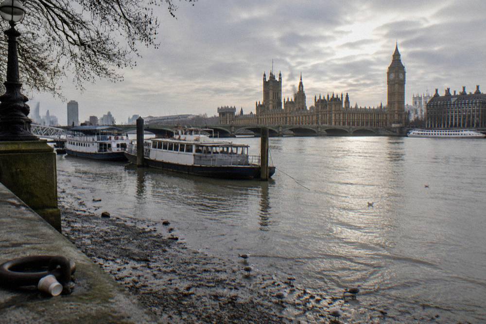 Thames riverside path with moored boats and winter sky above the water