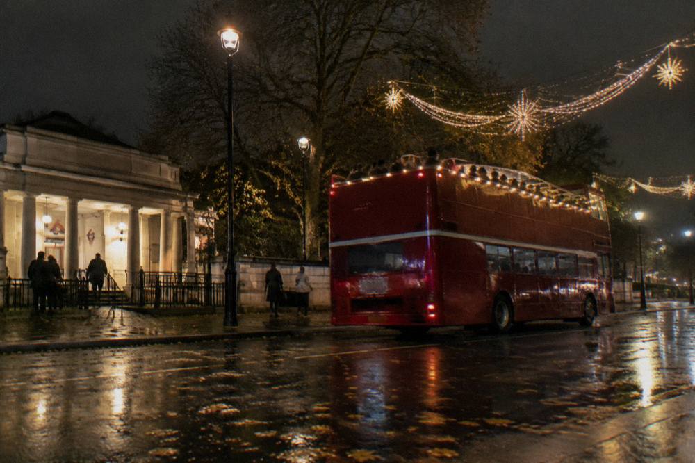 Open-top bus passing under illuminated Christmas lights on a London street at night