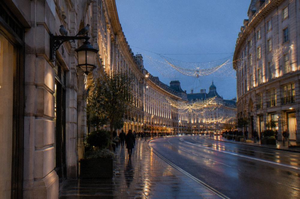 A narrow shopping street decorated with glowing Christmas light installations above evening shoppers