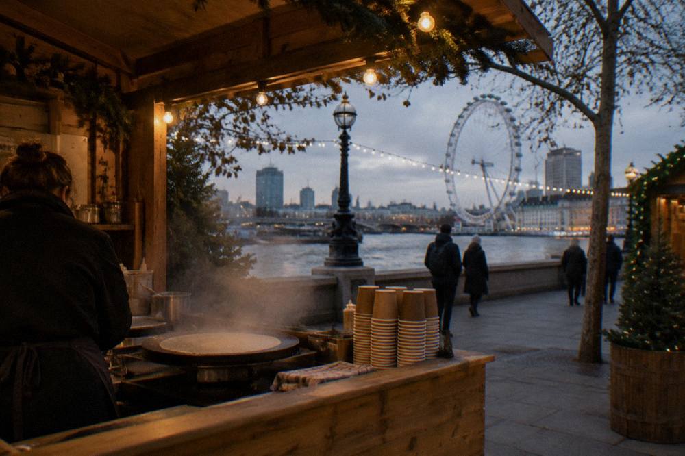 Illuminated Christmas market stalls along a riverside walkway in the evening