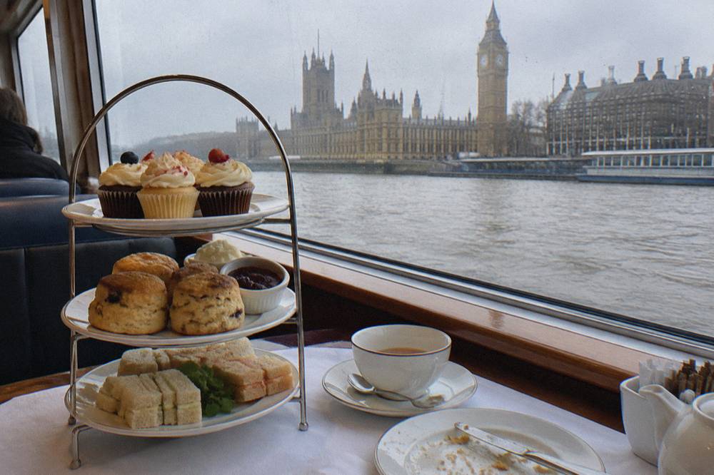 A tiered afternoon tea stand with scones and festive cupcakes beside a window overlooking the River Thames