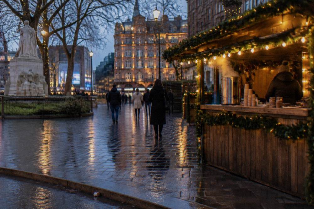 A Christmas market stall with garlands and warm lights in a London square in the early evening