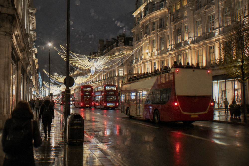 An open-top bus passing decorated buildings on a lit city street at night