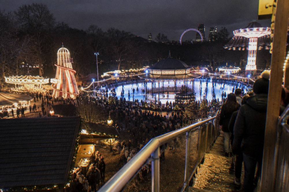 Illuminated fairground rides and a giant wheel glowing above a crowded winter park at dusk
