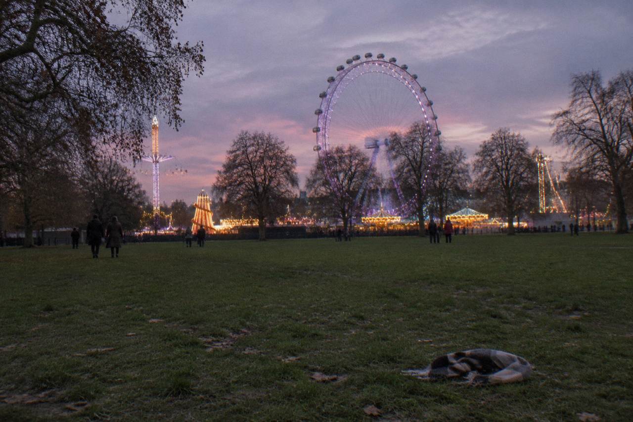 Ferris wheel and fairground rides illuminated against an evening sky in a London park