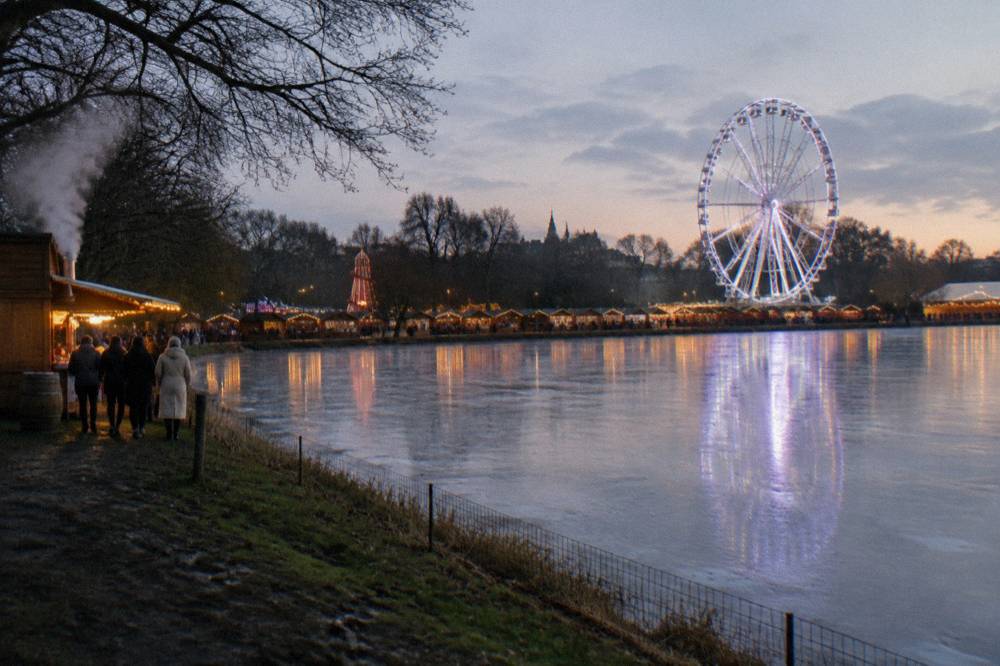 Winter market chalets and a ferris wheel lit up at dusk in a London park