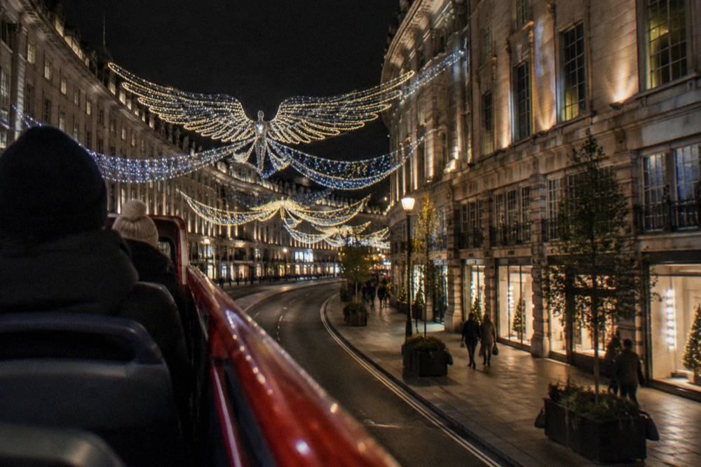 Open-top bus passing under illuminated Christmas lights on a city street at night