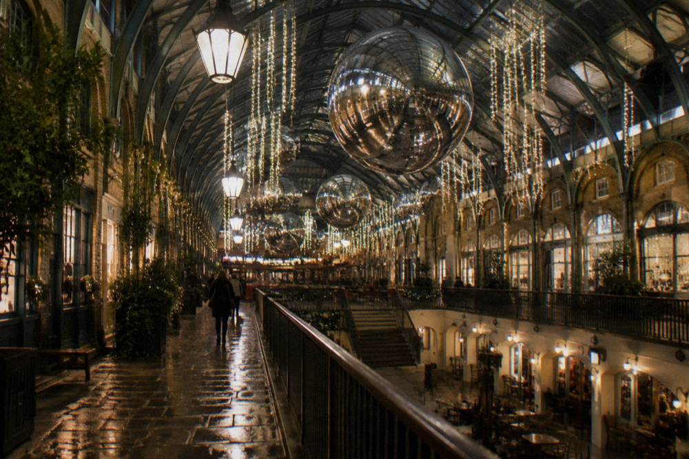 Illuminated Christmas lights strung across a London street above the rooftops of evening shops