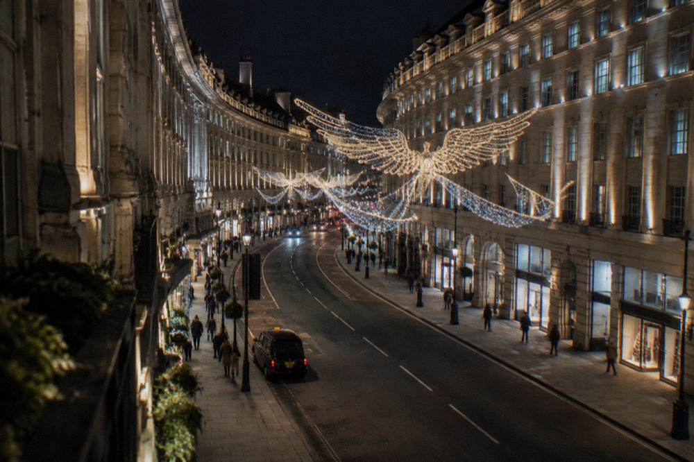 Illuminated Regent Street style shopping street with angel shaped Christmas lights at night
