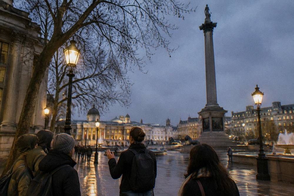 Small group of walkers with a guide on a lamp lit London street in the evening