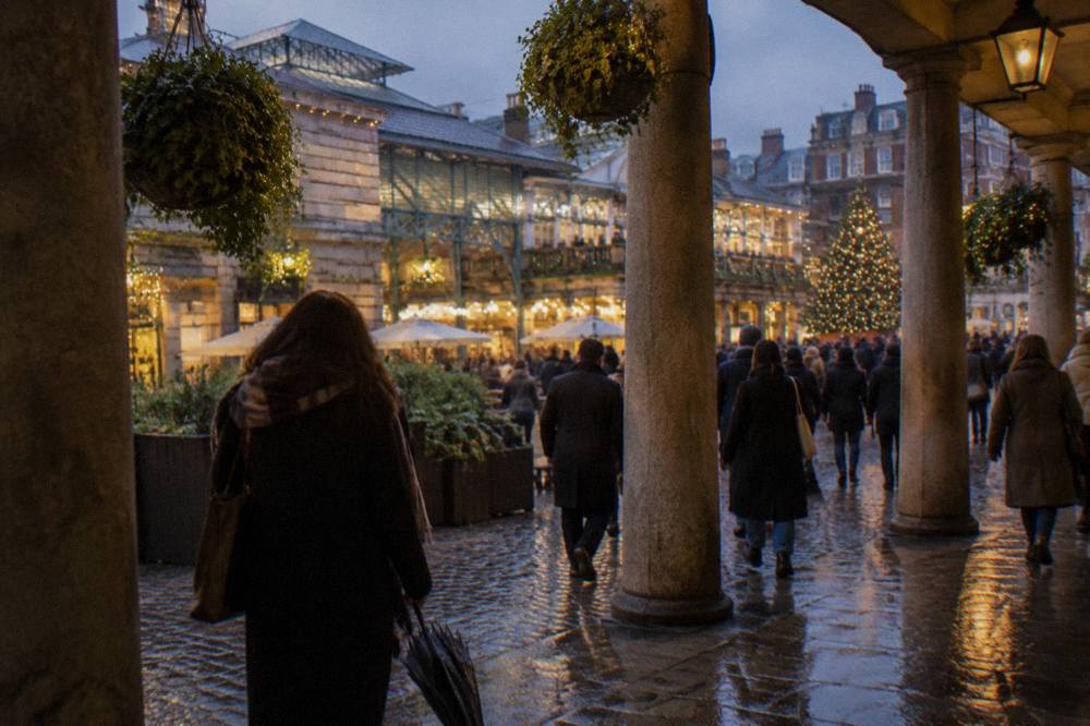 Crowd of people walking beneath glowing Christmas lights on a decorated London street in the evening
