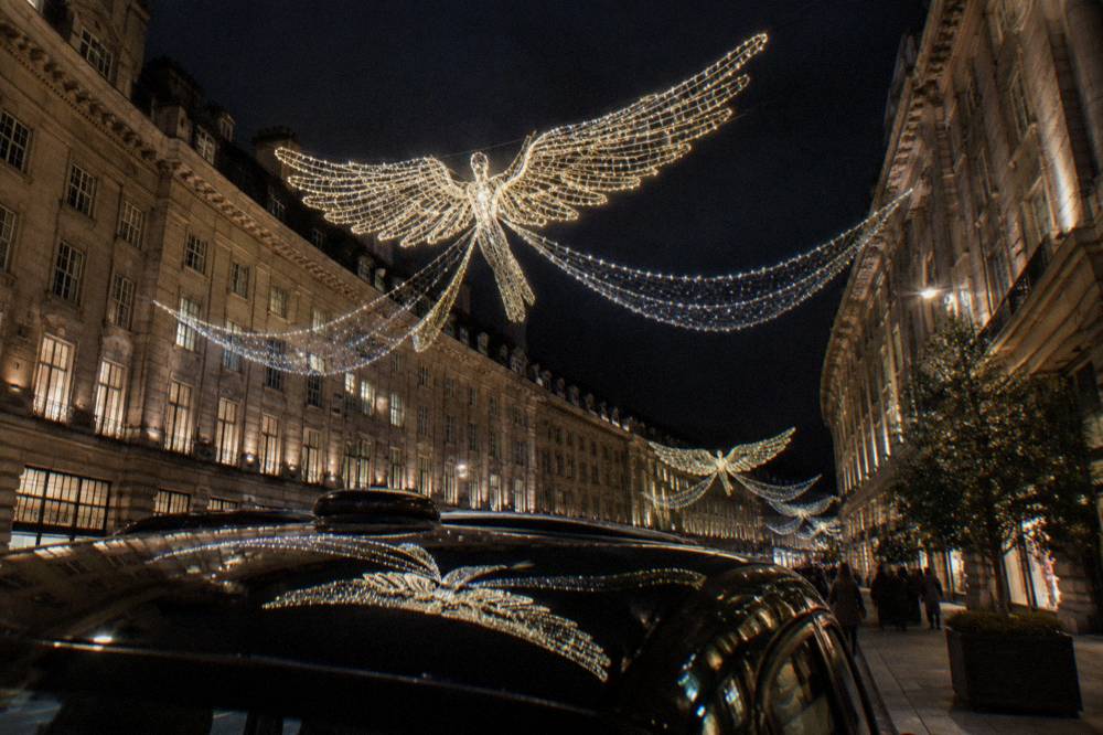Illuminated angel decorations suspended above a busy London shopping street after dark