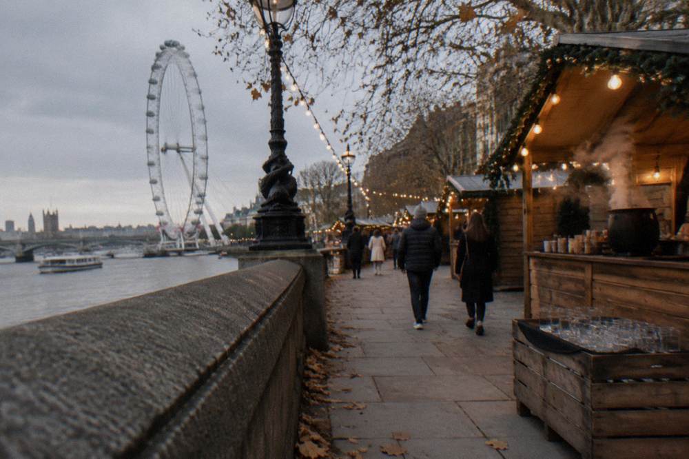 Wooden market chalets decorated with lights along a riverside walkway in London