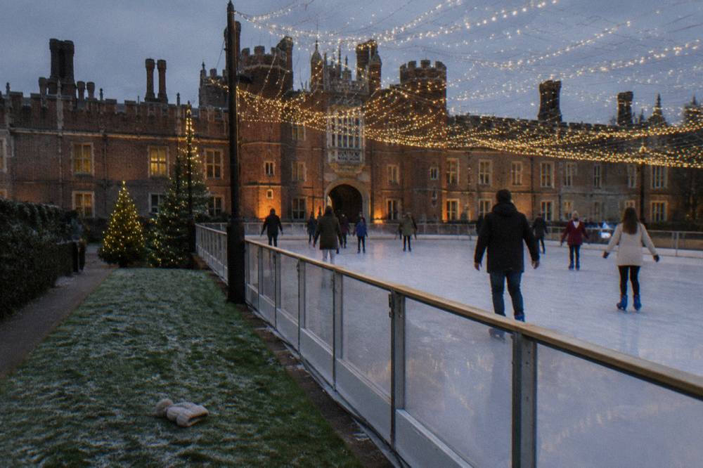 Skaters on an outdoor rink beside a floodlit palace facade with strings of lights overhead