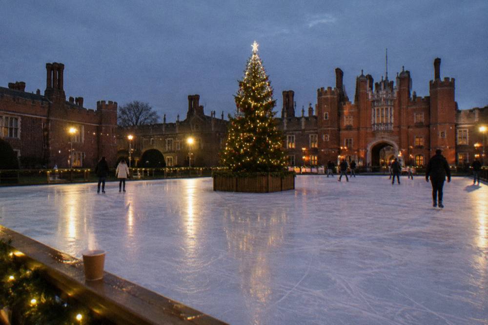 A Christmas tree glowing at the centre of an outdoor ice rink in a stone courtyard
