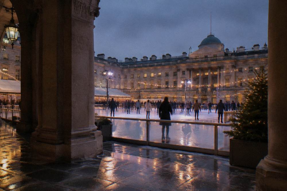Skaters in winter coats and gloves on an outdoor rink at night under string lights