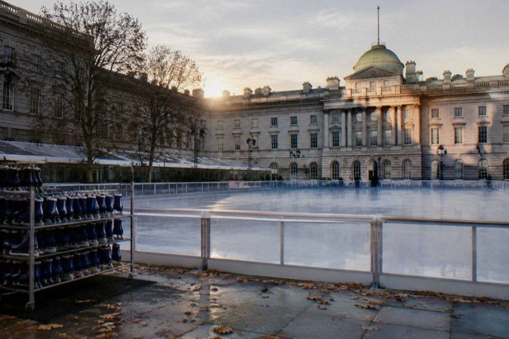 An empty outdoor ice rink in late afternoon light with a decorated tree beside it