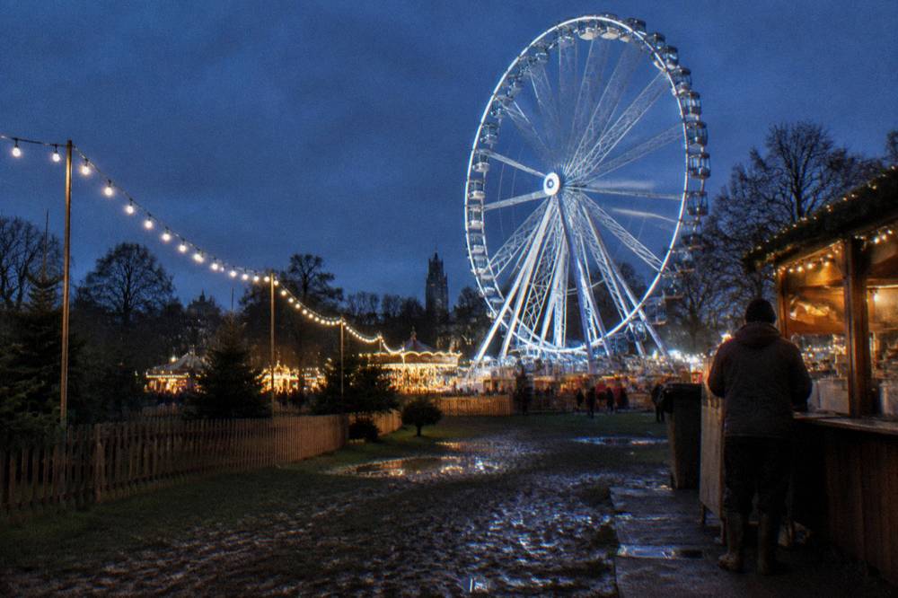 An illuminated winter fairground at night with a large Ferris wheel and string lights