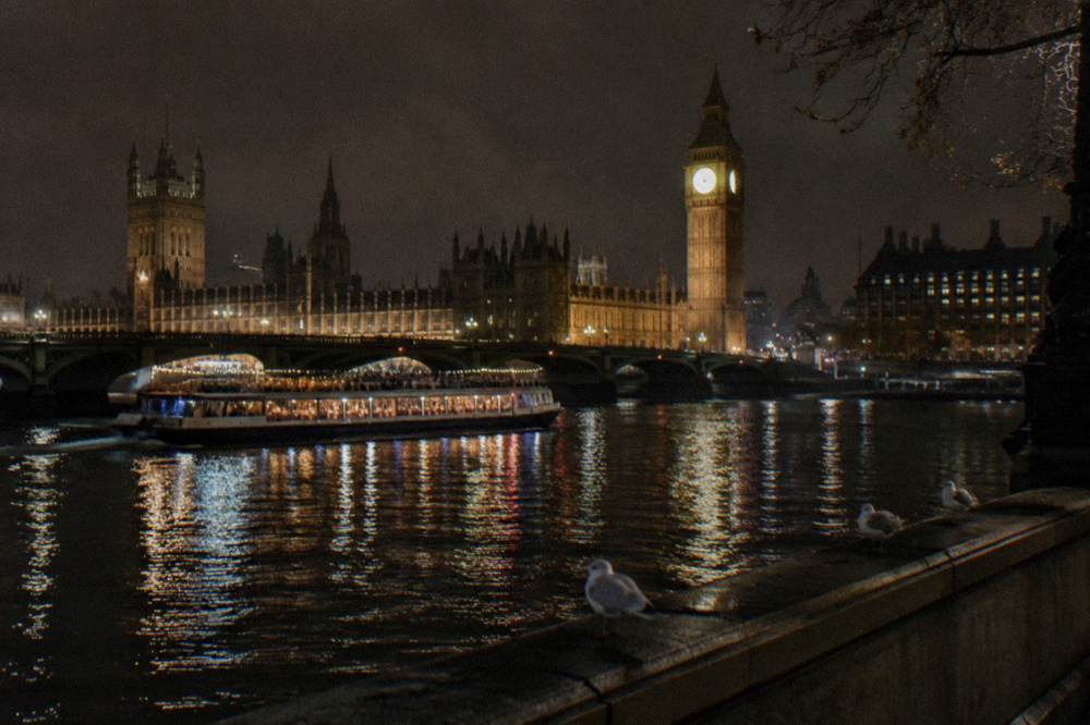 A river boat lit up at night passing illuminated bridges on the Thames