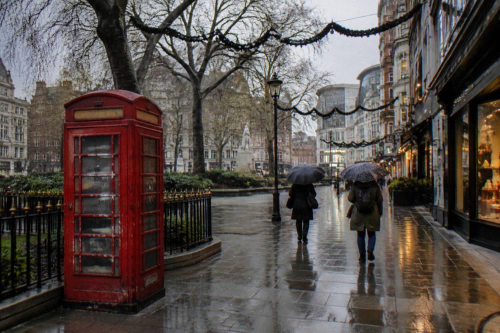 A quiet London street corner in early winter with a few pedestrians and lit shopfronts