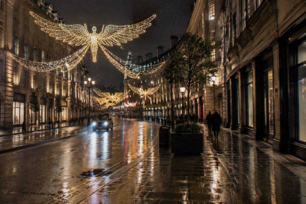 A wide London street at night with large illuminated angel decorations suspended across the road