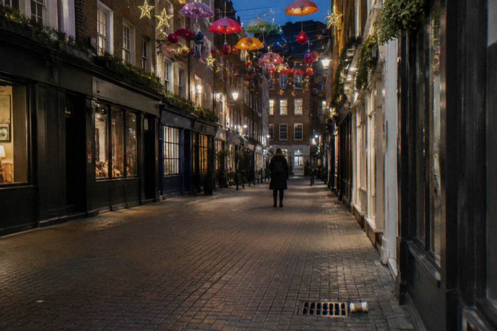 A pedestrian shopping lane in Soho at night lined with overhead festive decorations