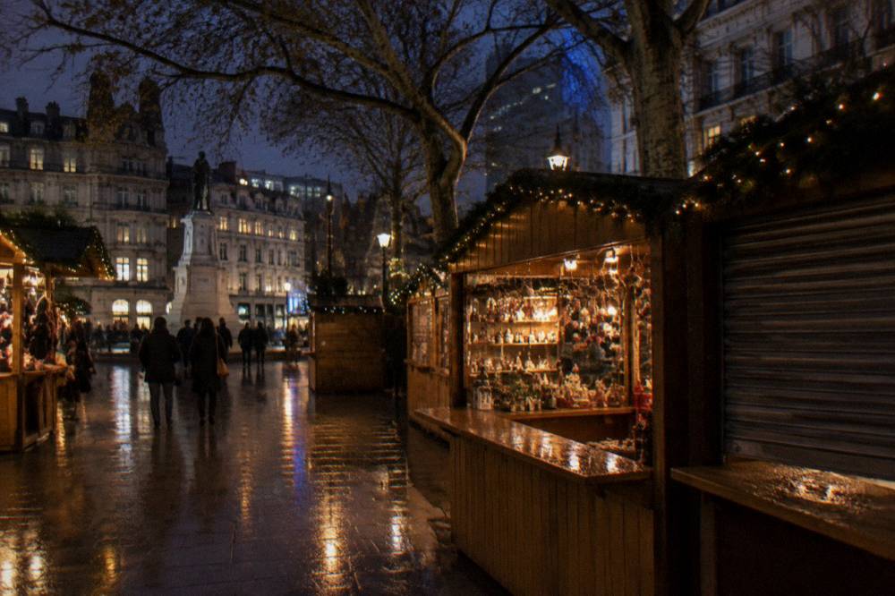 A small square of decorated market stalls glowing under trees in the evening