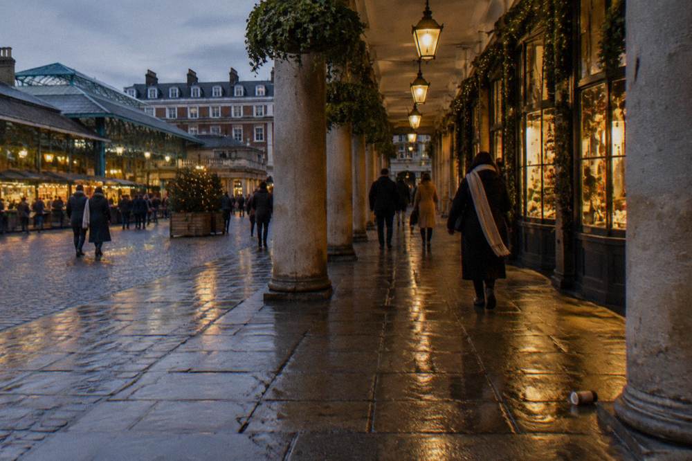 Coats and scarves on visitors walking past lit shop windows in London