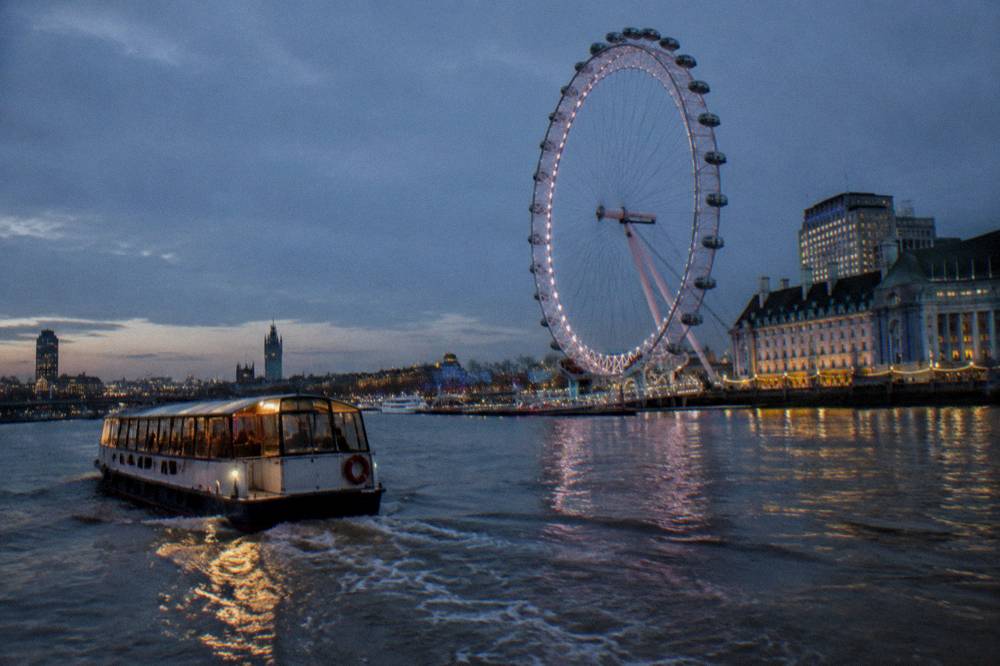 A river boat on the Thames at dusk passing illuminated buildings
