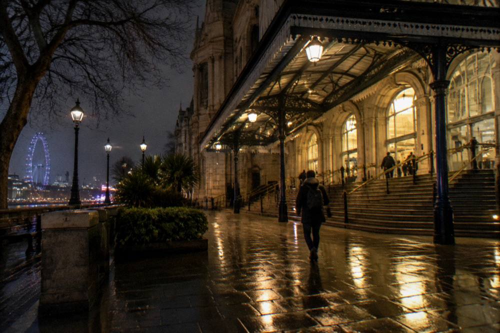 An Underground station entrance lit at night with rain-slicked pavement