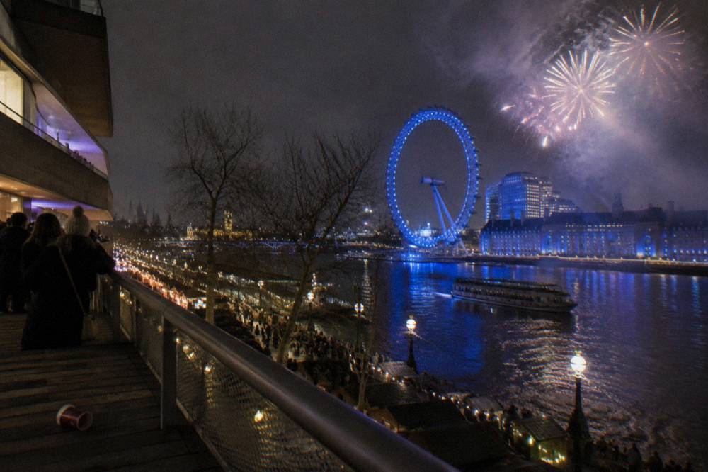Fireworks bursting over the Thames at night with the London Eye in the background