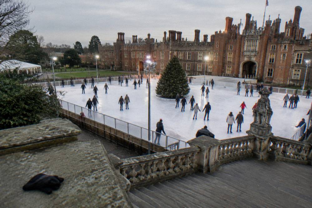 An outdoor ice rink in a floodlit historic courtyard with skaters and a large Christmas tree
