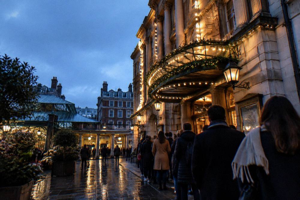 A grand theatre facade decorated with festive lights and a glowing marquee at dusk